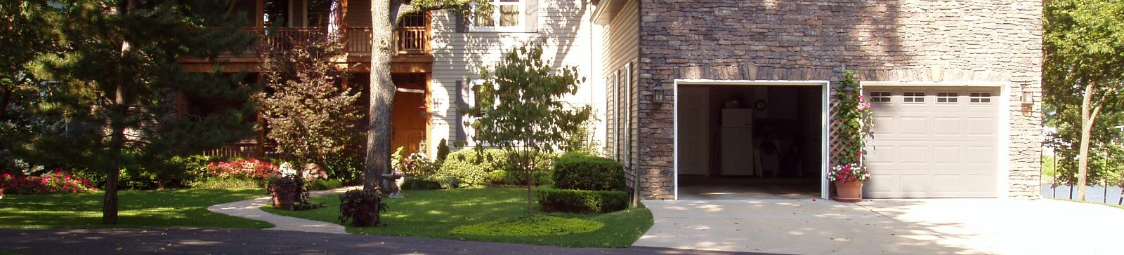 A well-maintained stone and siding home in Magna, Utah, featuring a double garage with one door open and lush landscaping in the front yard.