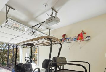 Spacious Magna garage interior with an automatic overhead door opener equipped with battery backup, a blue golf cart, and organized wall shelves.
