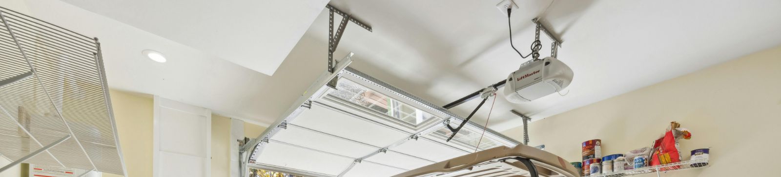 Spacious Magna garage interior with an automatic overhead door opener equipped with battery backup, a blue golf cart, and organized wall shelves.