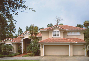 Spacious Kearns home with original plain beige garage doors and Mediterranean-style architecture, surrounded by palm trees and a manicured lawn.